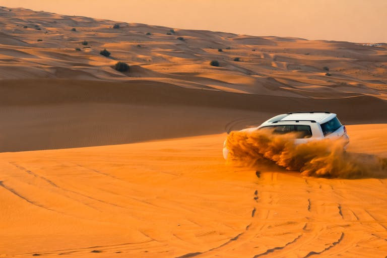 A thrilling SUV driving through the sand dunes of Dubai's desert landscape at sunset.