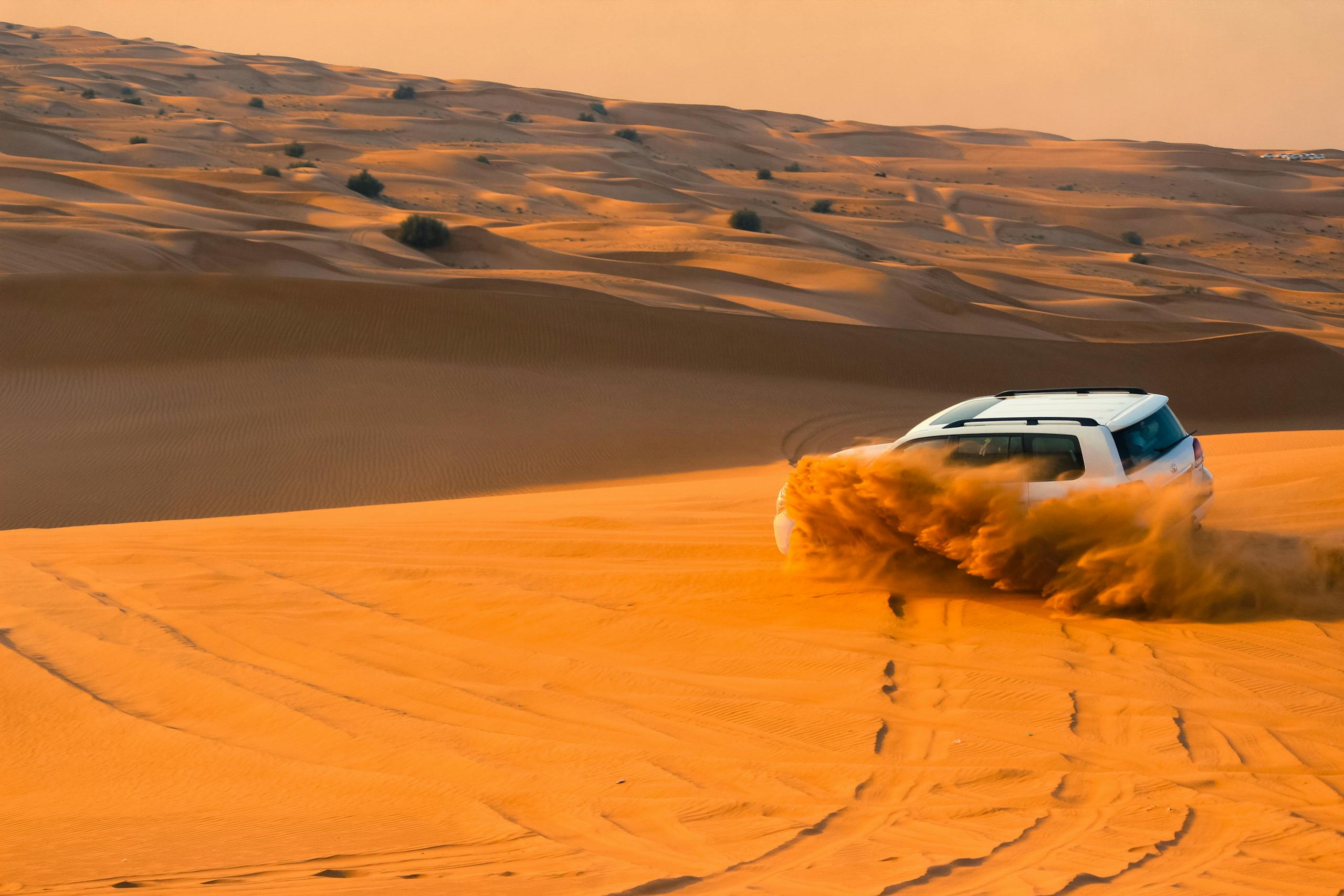 A thrilling SUV driving through the sand dunes of Dubai's desert landscape at sunset.